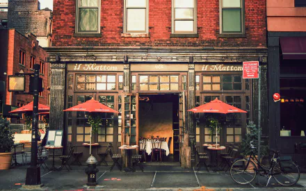 A charming restaurant exterior with a wooden facade and red umbrellas at outdoor tables, set against a backdrop of vibrant city life. An inviting HD desktop wallpaper.