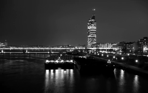 Black and white night view of Vienna cityscape in Austria, featuring illuminated bridges and a prominent high-rise building along the river, captured as a HD desktop wallpaper.