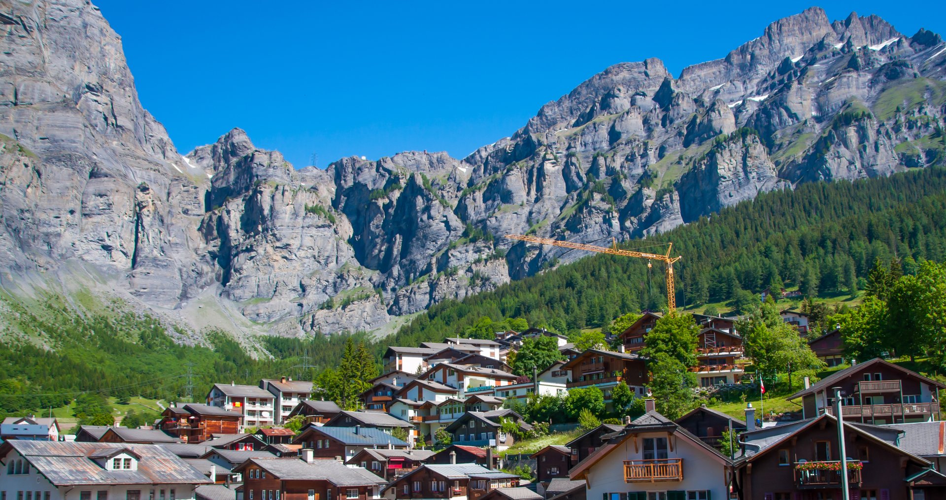 A scenic view of a village nestled among majestic mountains in Montreux, Switzerland, showcasing a blend of nature and man-made structures against a clear blue sky.