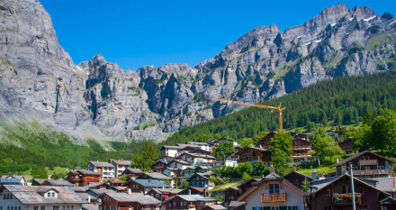 A scenic view of a village nestled among majestic mountains in Montreux, Switzerland, showcasing a blend of nature and man-made structures against a clear blue sky.