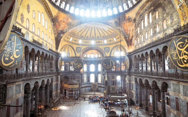 Interior view of Hagia Sophia, showcasing its magnificent architecture with grand arches, intricate mosaics, and large calligraphic medallions, creating a stunning religious atmosphere.