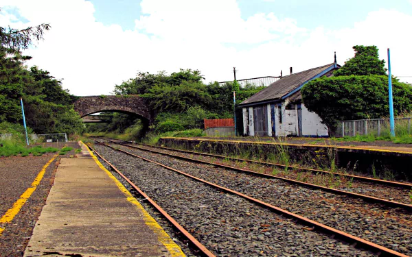 HD desktop wallpaper of a serene train station with railway tracks, a bridge, and a small white building surrounded by lush greenery.