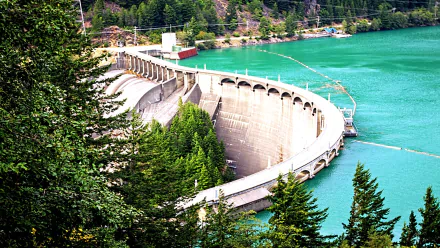A stunning HD image of a man-made dam nestled among lush greenery, surrounded by vibrant turquoise water, showcasing the harmony between engineering and nature.