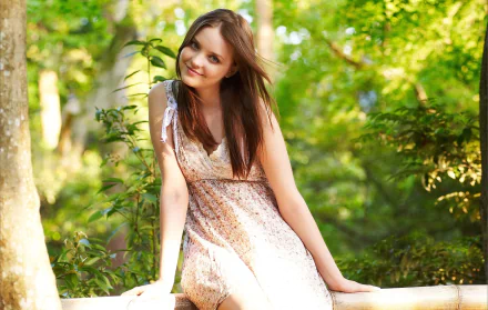 A woman in a light dress smiles while sitting on a wooden fence, surrounded by lush green trees in a serene outdoor setting. HD desktop wallpaper and background.