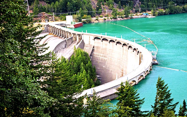 A stunning HD image of a man-made dam nestled among lush greenery, surrounded by vibrant turquoise water, showcasing the harmony between engineering and nature.