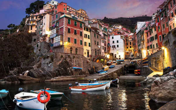 HD desktop wallpaper showcasing the man-made colorful buildings and boats of Riomaggiore at dusk, nestled along the rocky coastline.
