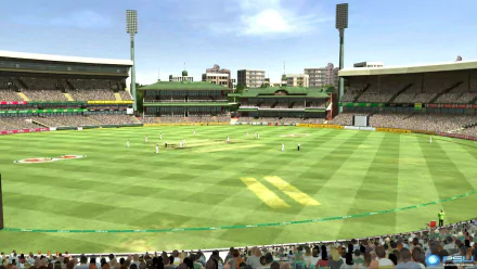 HD wallpaper of a cricket stadium filled with spectators, featuring a bright green field under a clear sky, with players and structures in the background, capturing a lively match atmosphere.