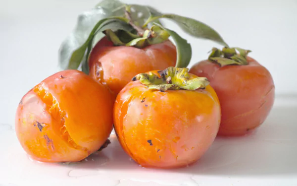 HD PC desktop wallpaper: close-up of ripe orange persimmons with green leaves on a white background, food photography.