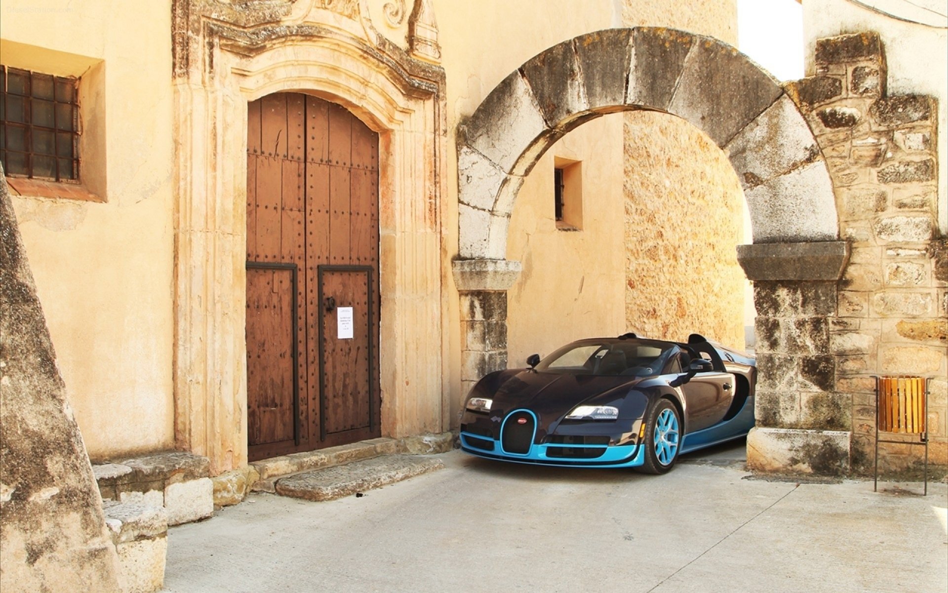 HD PC desktop wallpaper featuring a sleek Bugatti sports car parked beside an old stone arch and rustic building entrance.