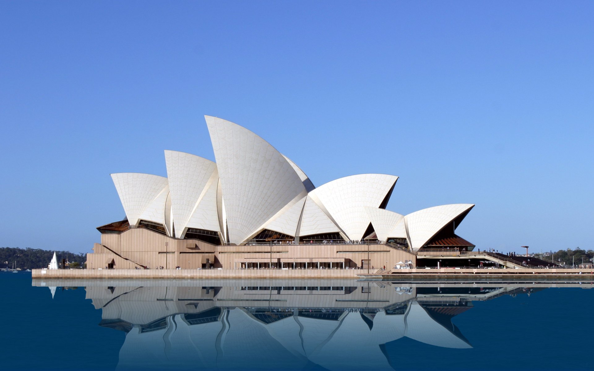 HD desktop wallpaper of the Sydney Opera House, a man-made architectural icon, set against a clear blue sky with its reflection on the calm water.