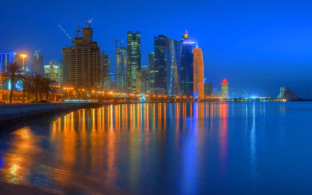 HD desktop wallpaper of Doha's skyline at night, featuring illuminated skyscrapers and their reflections on a calm waterfront.