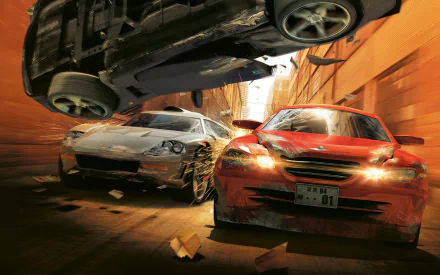 HD wallpaper featuring intense action from Burnout Revenge, showcasing a dramatic car chase with a flipped vehicle and a red car racing through a narrow alley.