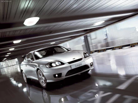 HD PC desktop wallpaper of a silver Hyundai Coupe vehicle in a glossy modern parking garage, motion blur and city skyline visible through side openings.