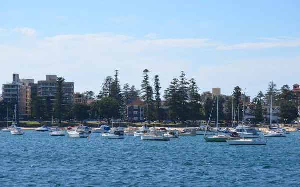 HD desktop wallpaper showing boats anchored near man-made buildings and trees along the Sydney Manly coastline under a bright blue sky.