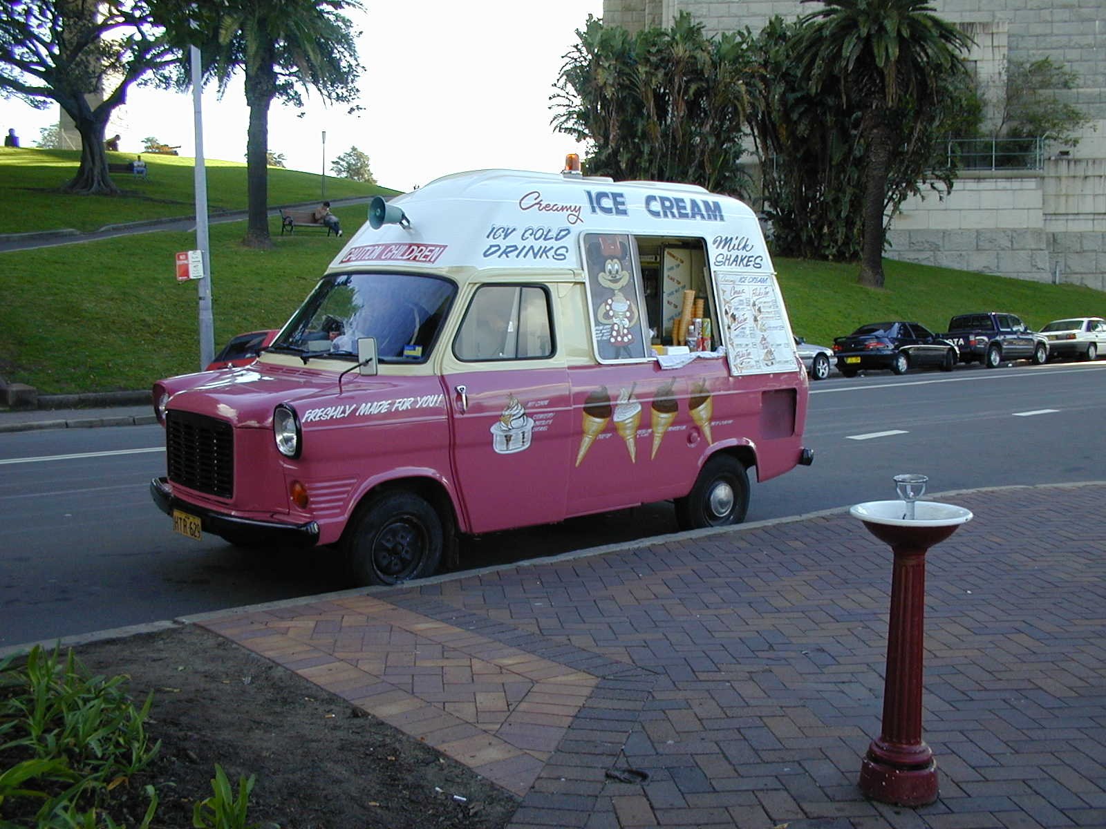 HD desktop wallpaper featuring a vintage pink and white ice cream truck parked on a street near a park.