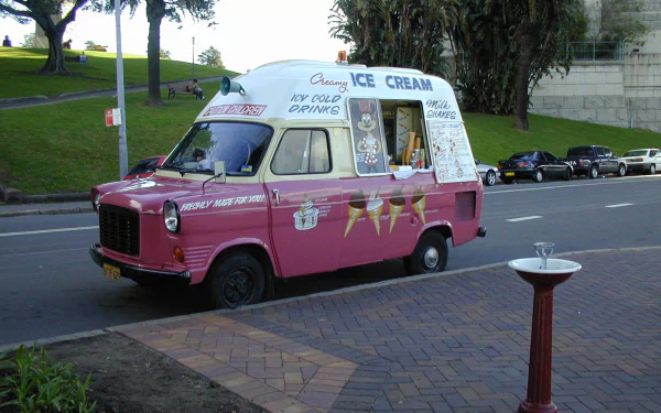 HD desktop wallpaper featuring a vintage pink and white ice cream truck parked on a street near a park.
