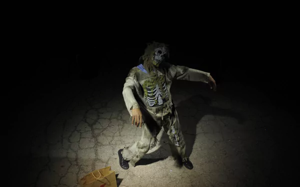 A 4K Ultra HD Halloween-themed PC desktop wallpaper depicting a person in a zombie costume crawling on a cracked surface with dark, eerie lighting.