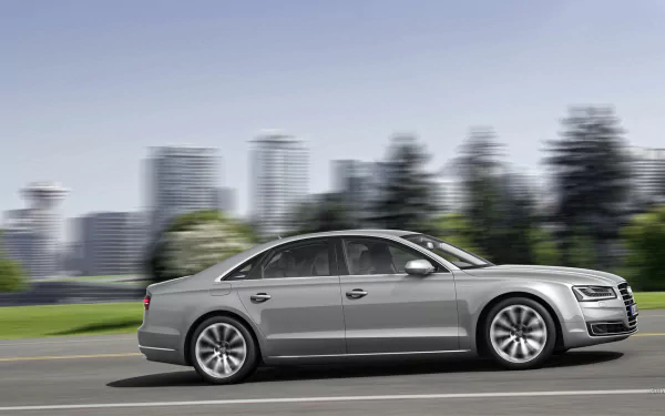 A sleek Audi A8 glides smoothly down a road with a modern city skyline in the background, all captured in a vibrant HD desktop wallpaper.