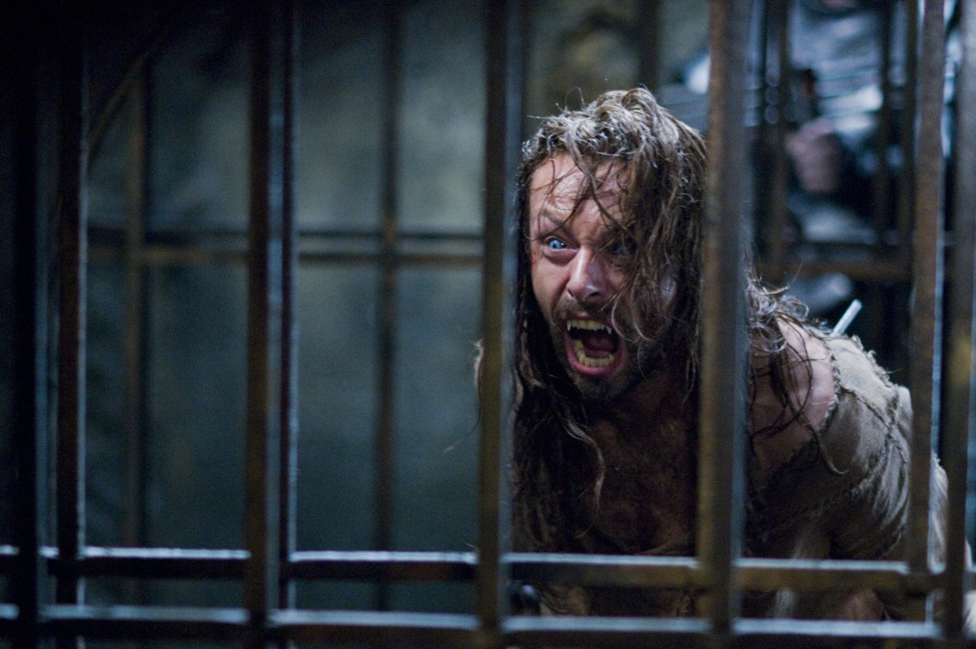 HD PC desktop wallpaper from the movie Underworld: Rise of the Lycans, showing a fierce, wild-haired man screaming behind metal bars in a dark, intense scene.