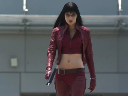 Milla Jovovich as the fierce protagonist in Ultraviolet, strides confidently in a striking red outfit, wielding a weapon against a futuristic backdrop. HD PC desktop wallpaper.