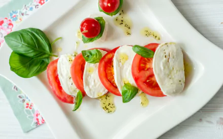 2K Quad HD PC desktop wallpaper/background: overhead caprese salad — alternating tomato and mozzarella slices with basil leaves and a drizzle of olive oil on a white plate (food, salad).
