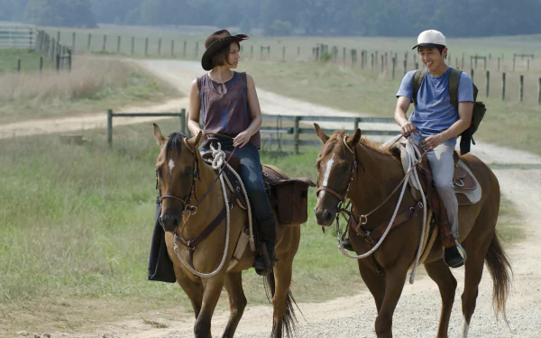 Maggie Greene and Glenn Rhee, portrayed by Lauren Cohan and Steven Yeun, ride horses along a dirt road in this HD wallpaper from The Walking Dead.
