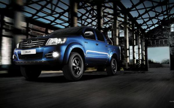 HD PC desktop wallpaper featuring a blue Toyota Hilux vehicle parked inside an industrial-style building with steel beams and large windows.