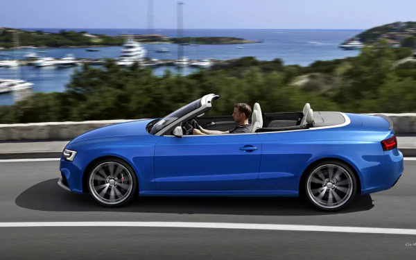 Blue Audi RS5 convertible driving along a coastal road by a marina, sea horizon in view — HD PC desktop wallpaper/background