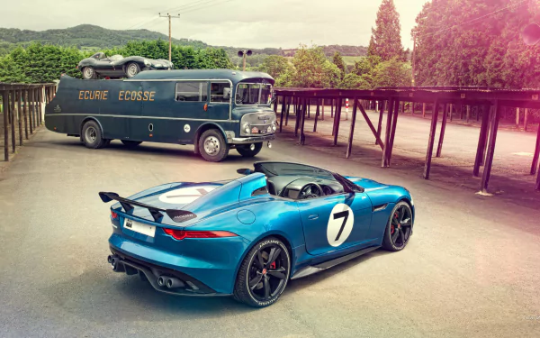 HD PC desktop wallpaper: blue 2013 Jaguar Project 7 Concept roadster with white '7' decal parked beside a vintage bus in a sunlit lot with trees and hills.