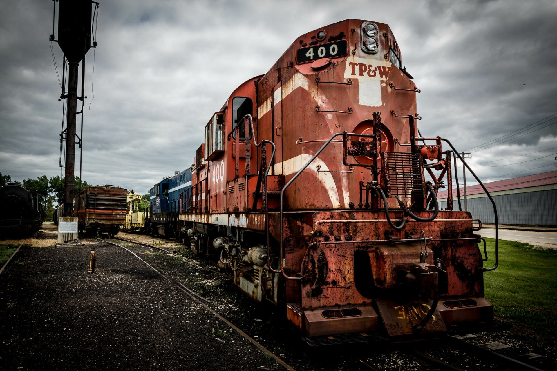 HD desktop wallpaper featuring a vivid image of a red and weathered TP&W train locomotive parked on tracks under a cloudy sky.