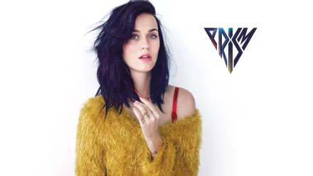 A high-definition desktop wallpaper featuring Katy Perry with dark hair, wearing a fuzzy yellow sweater, alongside the PRISM logo.