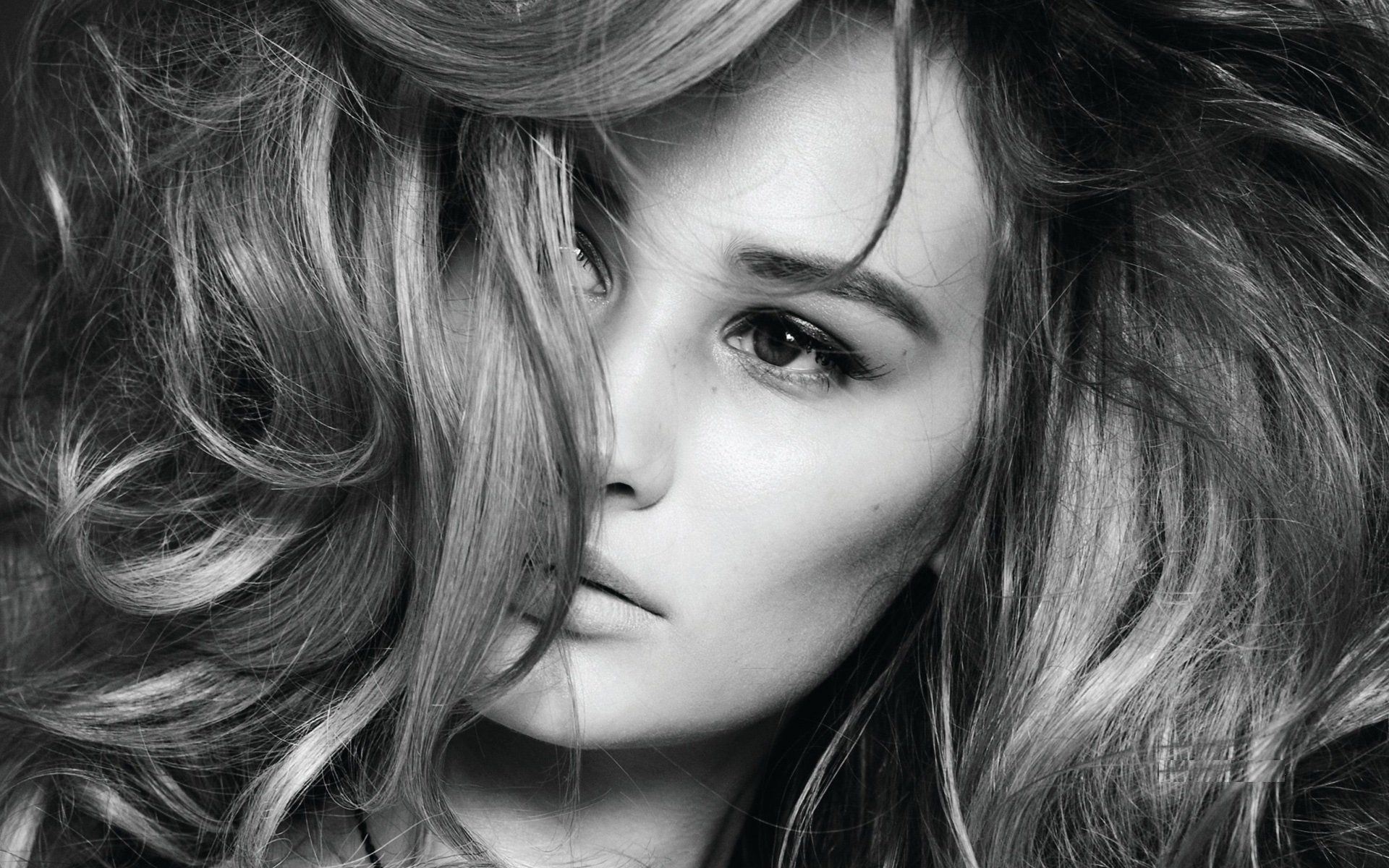 Black-and-white close-up of a woman with voluminous hair and a pensive gaze; identity not provided. HD PC desktop wallpaper/background.