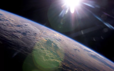 HD desktop wallpaper showing Earth from space with sunlight shining over the planet’s curved horizon, highlighting clouds and the atmosphere against the dark background of space.