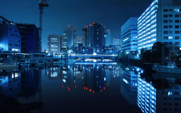 Nighttime view of Tokyo’s cityscape with illuminated skyscrapers reflected on calm water, showcasing a man-made urban environment in high-definition detail.