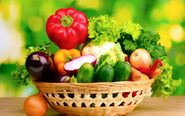 A vibrant basket of fresh vegetables, including bell peppers, cucumbers, and lettuce, set against a blurred green background, featuring a lively, healthy food theme.