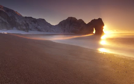Sunset at Durdle Door showcasing natural coastal rock formations with waves gently washing onto the sandy shore, captured in stunning HD for a desktop wallpaper.