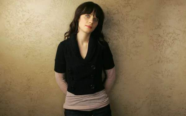 Zooey Deschanel poses casually against a textured background, showcasing her signature style. This high-definition image serves as a captivating desktop wallpaper.