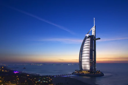 4K Ultra HD image of the man-made Burj Al Arab luxury hotel illuminated at dusk against a serene coastal skyline and deep blue sky.