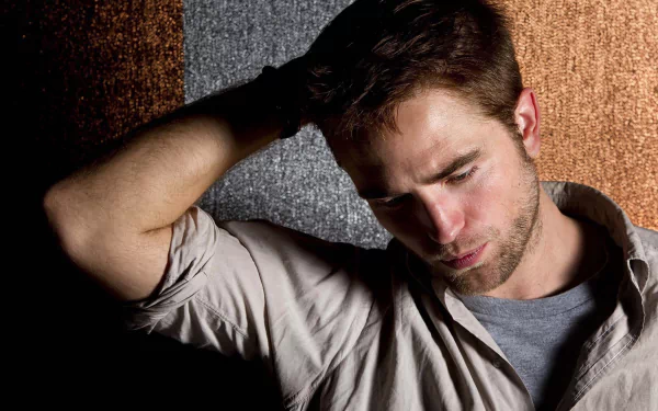 A contemplative Robert Pattinson with a beard poses against a textured backdrop, creating a striking desktop wallpaper for fans and admirers.