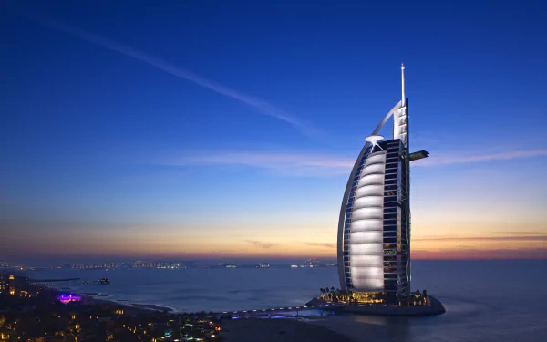 4K Ultra HD image of the man-made Burj Al Arab luxury hotel illuminated at dusk against a serene coastal skyline and deep blue sky.