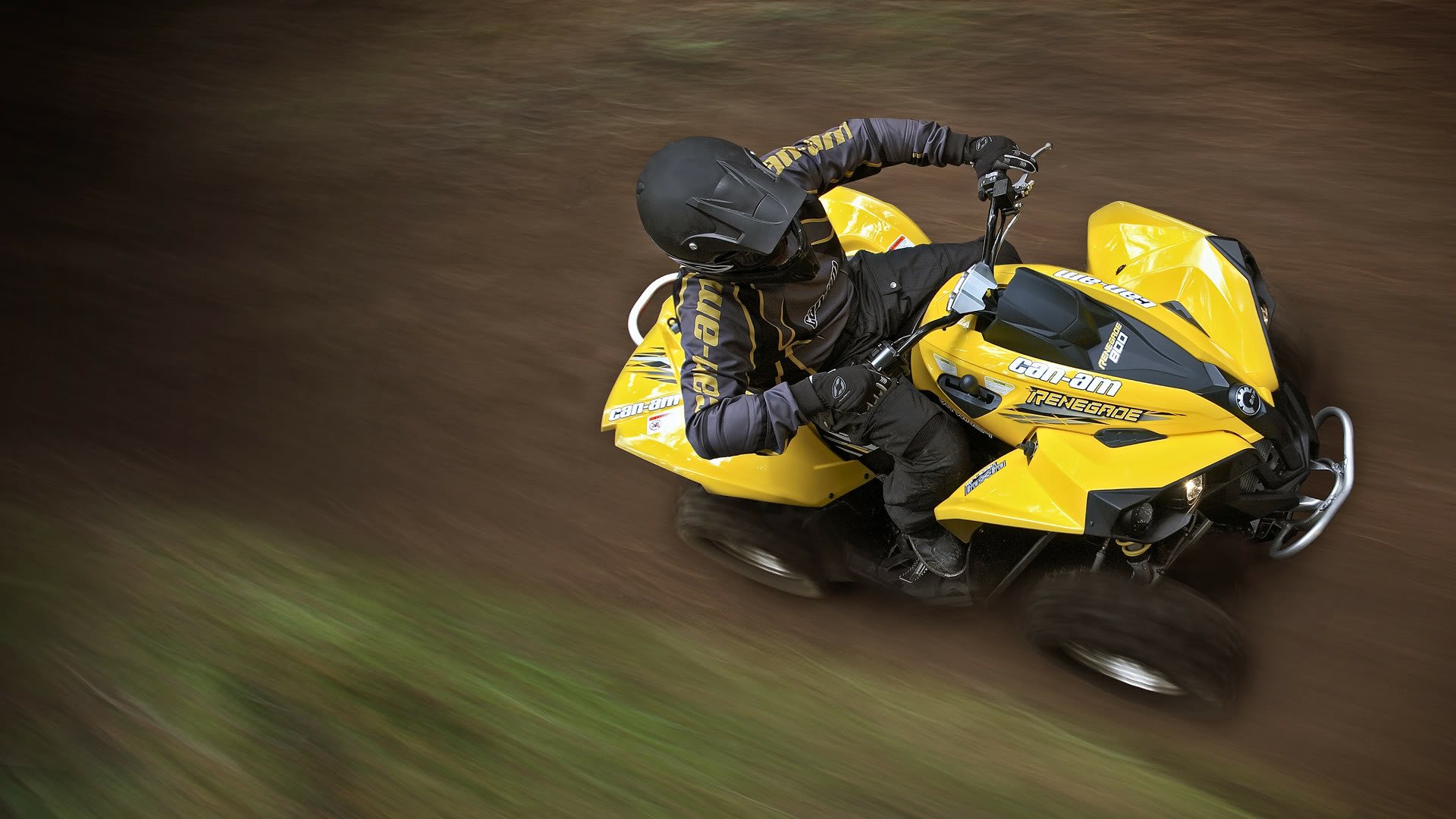 High-definition PC desktop wallpaper featuring a dynamic Can-Am vehicle in motion, ridden by a helmeted driver on an off-road trail.