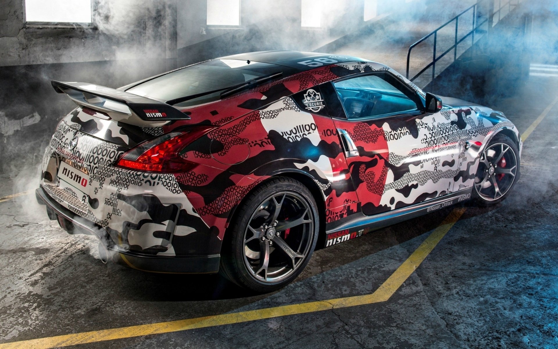 HD PC desktop wallpaper featuring a Nissan 370Z with a striking red, black, and white camo design parked in an industrial setting with smoke effects.