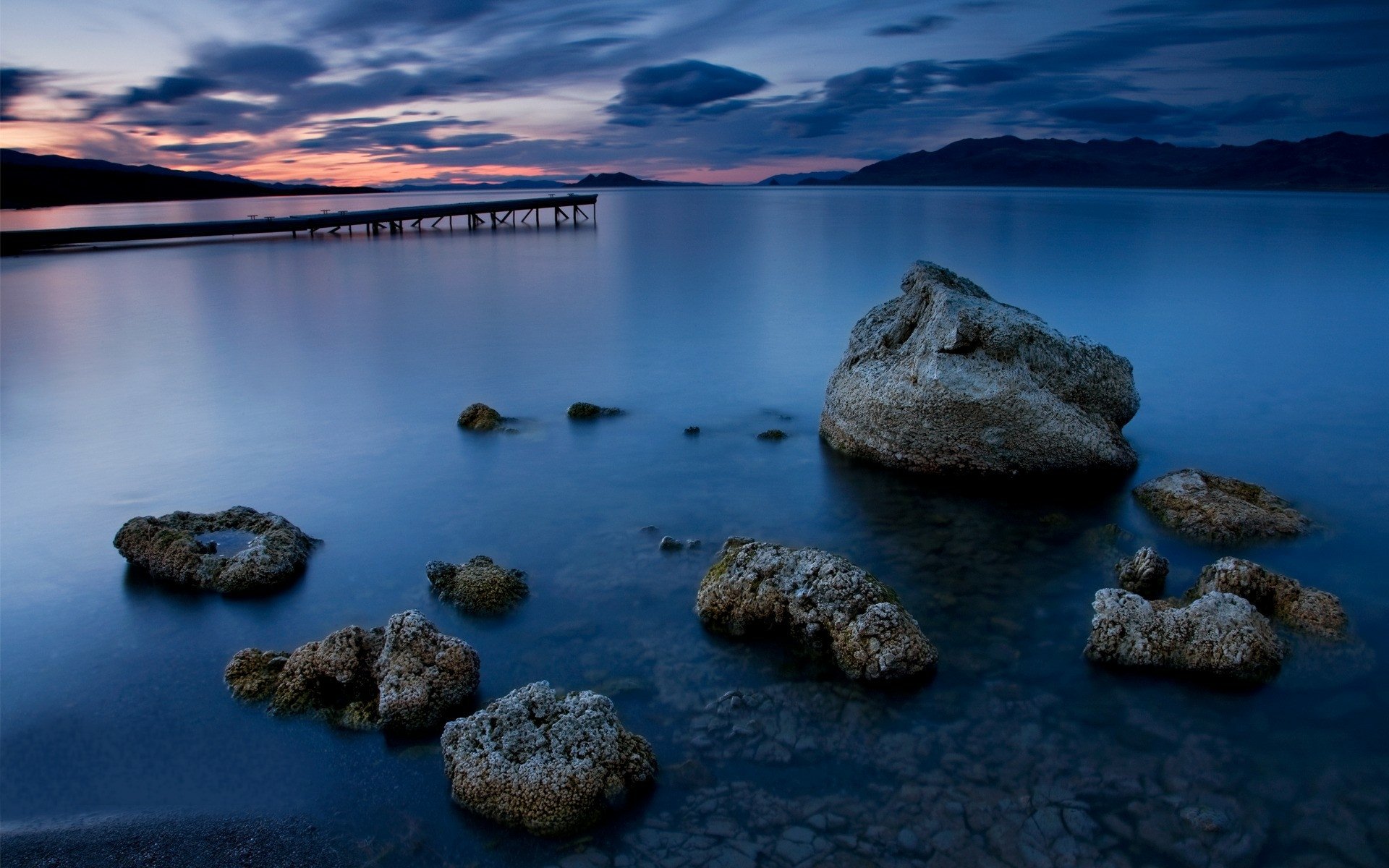 HD PC desktop wallpaper showcasing a serene ocean scene at dusk with rocky formations in calm water under a vibrant, colorful sky.