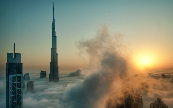 A stunning HD desktop wallpaper showcasing Dubai's skyline, featuring the Burj Khalifa rising above a sea of clouds at sunrise, with a warm glow illuminating the scene.
