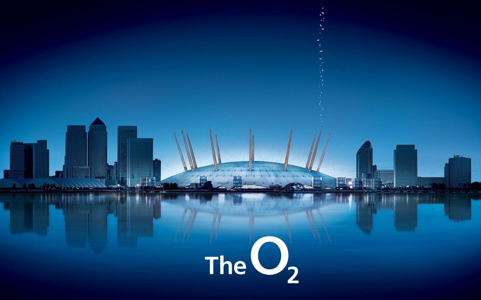 HD PC desktop wallpaper/background of London's man-made skyline centered on The O2 arena, reflected across a calm river in deep blue tones.