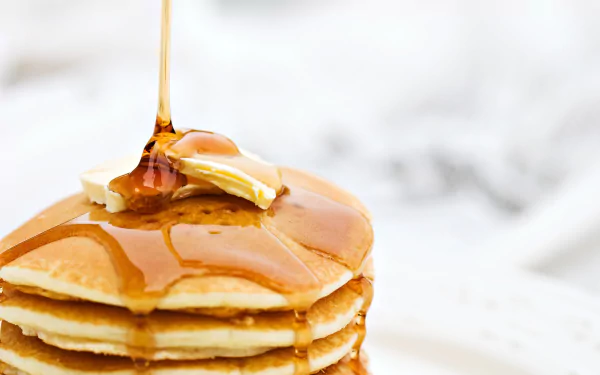A close-up of stacked pancakes drizzled with syrup and topped with a pat of butter, set against a soft, neutral background, making it an enticing HD desktop wallpaper.