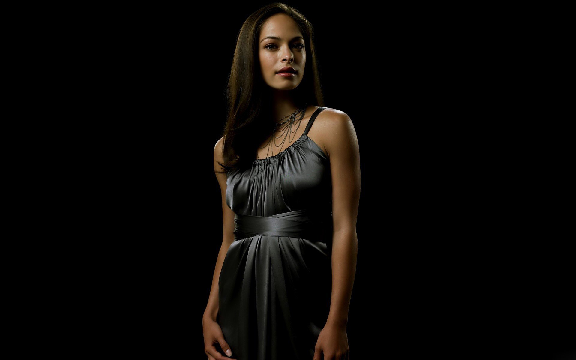 A striking HD desktop wallpaper featuring celebrity Kristin Kreuk in a stylish gray dress, set against a dramatic black background.