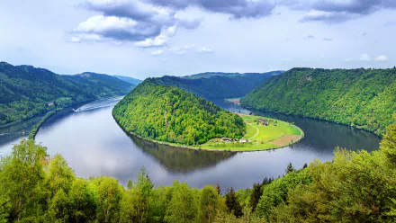HD desktop wallpaper featuring the Danube River winding through lush greenery and hills under a partly cloudy sky, showcasing the serene beauty of nature.
