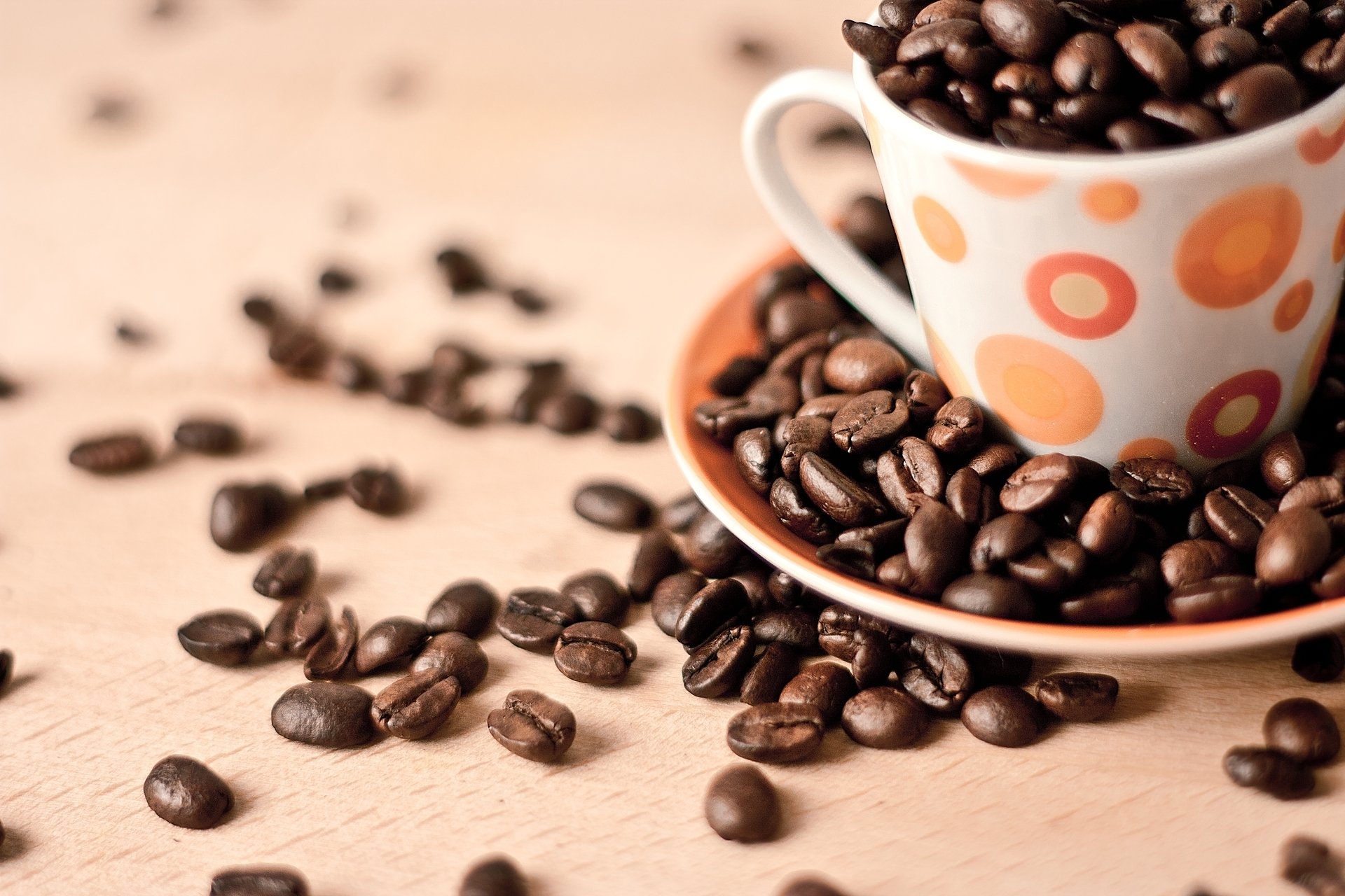 HD PC desktop wallpaper featuring a close-up of a coffee cup filled and surrounded by roasted coffee beans on a light wooden surface.
