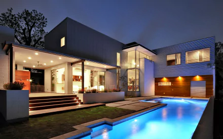 A modern house illuminated at night, featuring sleek architecture and a glowing pool, set in a serene landscape. This HD image serves as a striking desktop wallpaper.